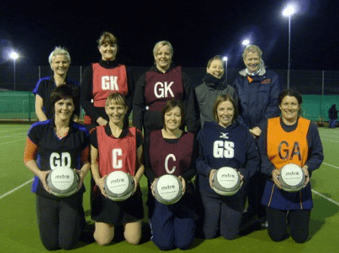 A netball team in position bibs on an outdoor court at night